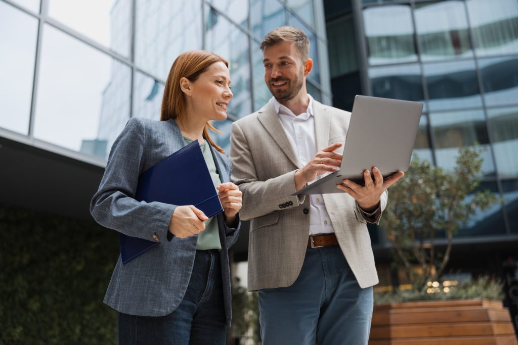 Two business professionals discussing project details on a laptop outdoors.